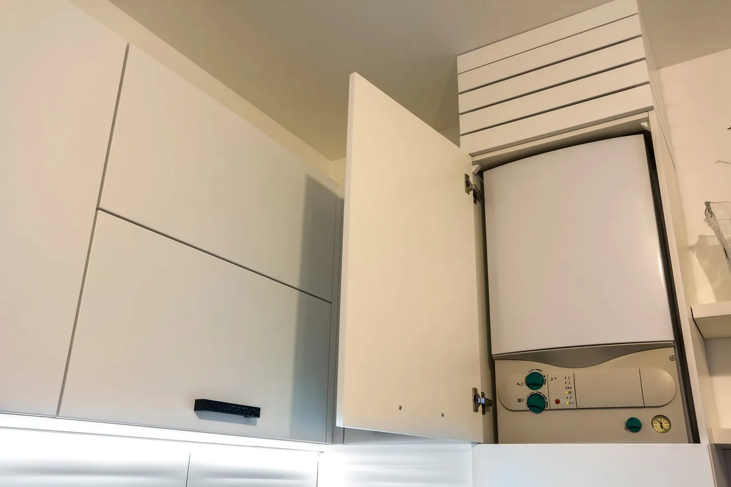 A white combi boiler fitted inside a kitchen wall cabinet, with the cabinet door open