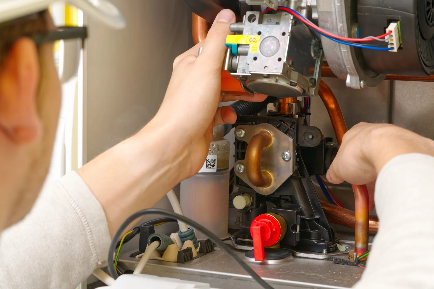 An engineer's hands working on the gas valve and pipework inside an open boiler
