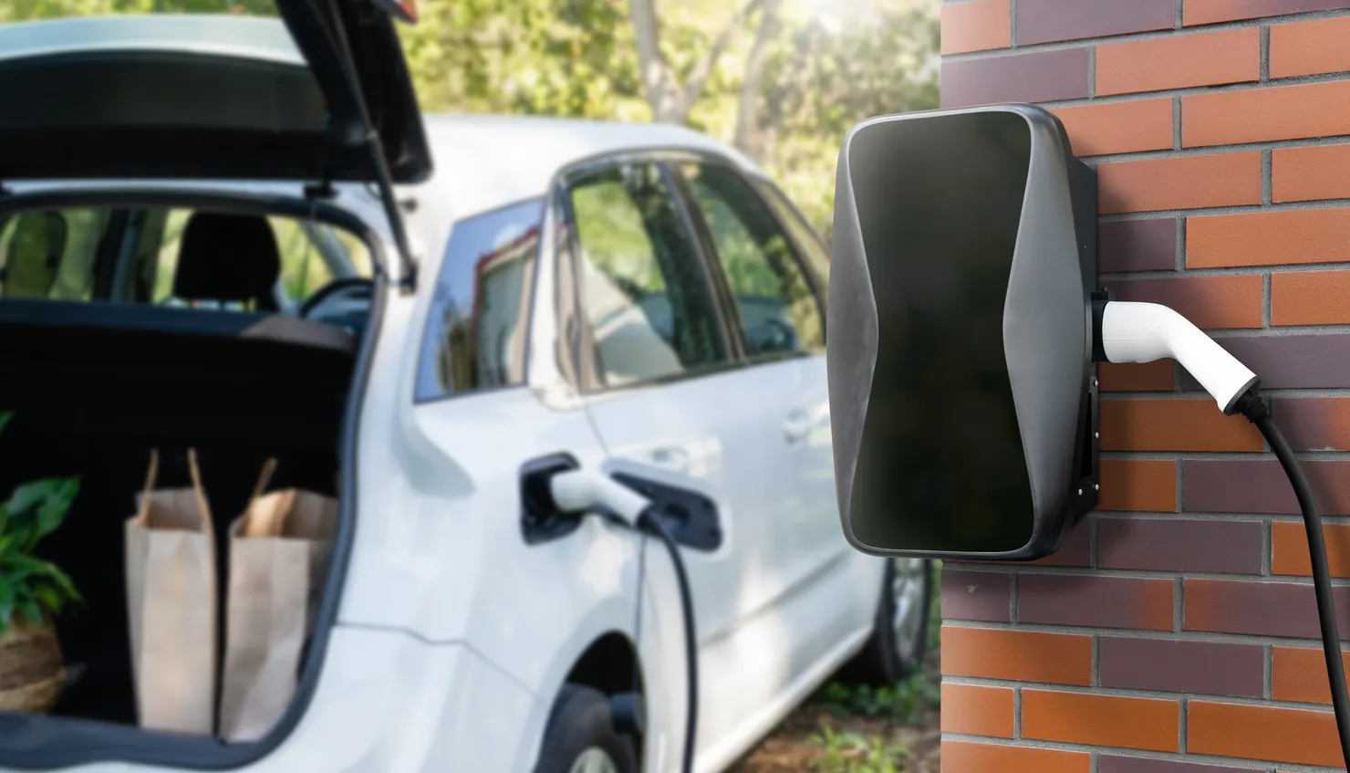 Home EV charger mounted on a brick wall charging an electric car on the driveway