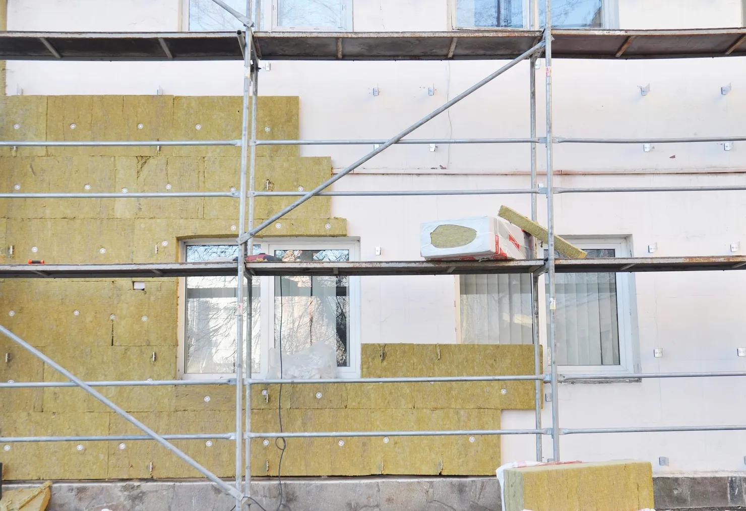 Mineral wool insulation boards being fixed to the outside wall of a house behind scaffolding